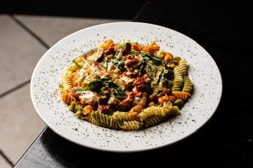 A complete plate of rotini pasta with chicken, spinach, and tomatoes